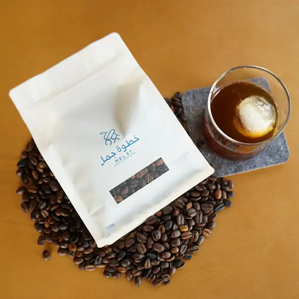 Colocação plana do saco de café sobre grãos de café torrados ao lado do café gelado para apresentação do produto