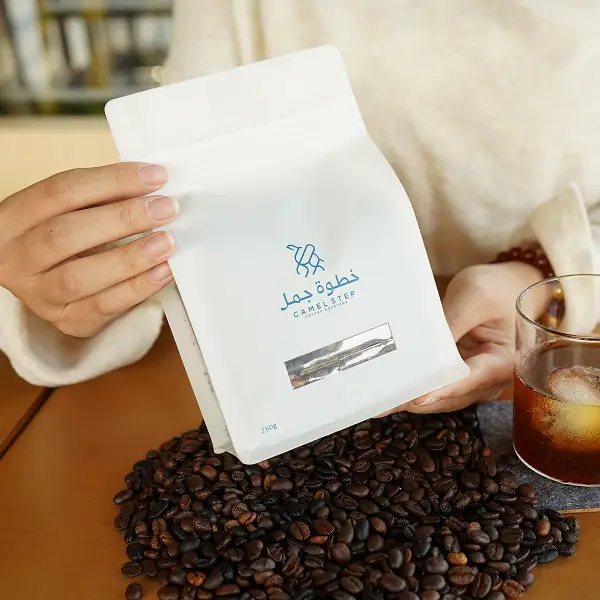 Cliente segurando um saco de café branco com uma caixa de papel impressa em um ambiente de estilo de vida